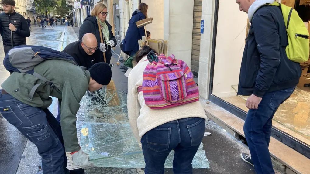 Des habitants aident un commerçant à ramasser les débris de sa vitrine