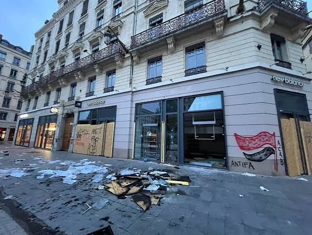 Rue commerçante au petit matin, devantures barricadées et débris sur le trottoir